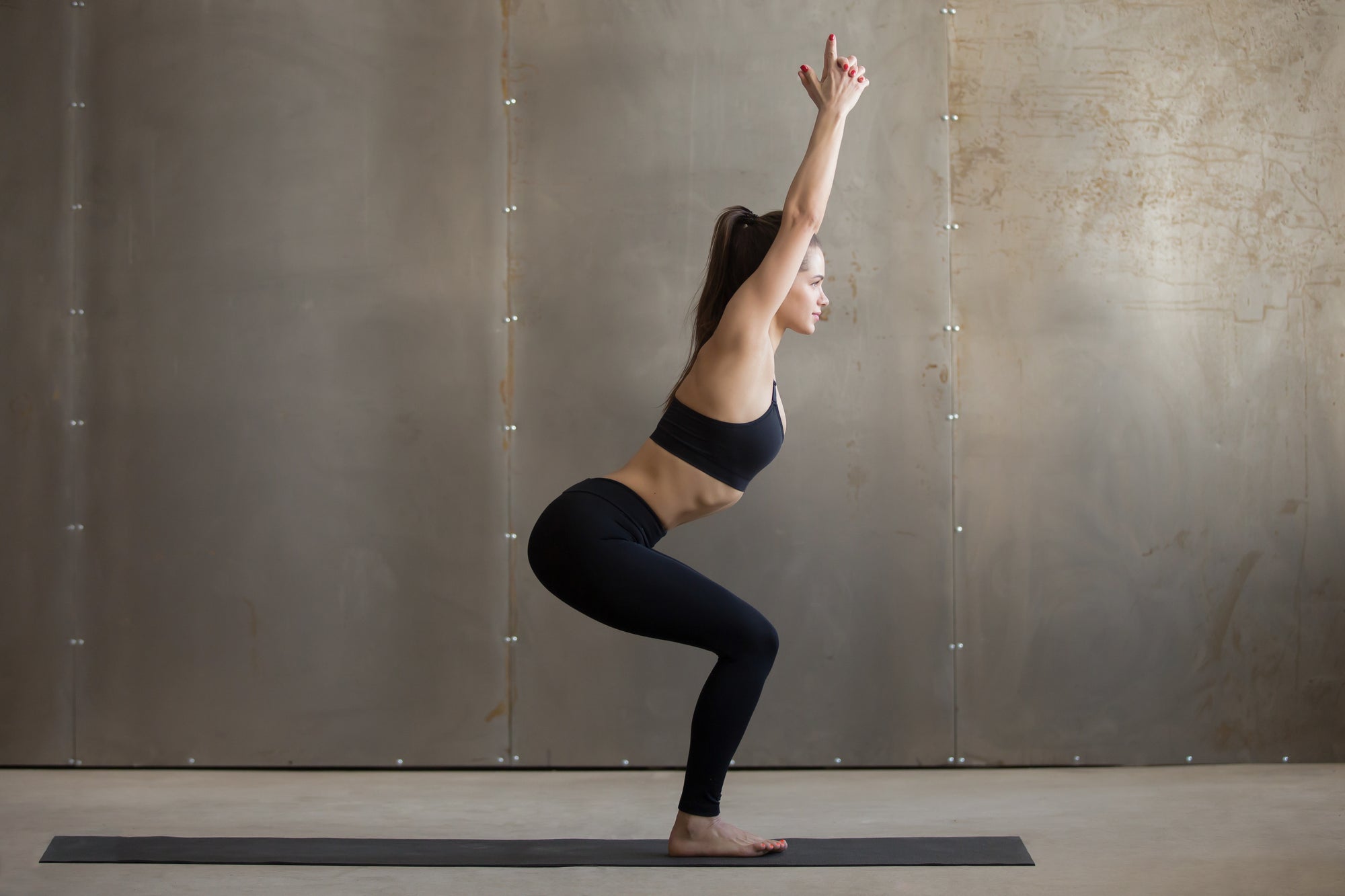 Young woman practicing yoga standing in Utkatasana exercise, Chair